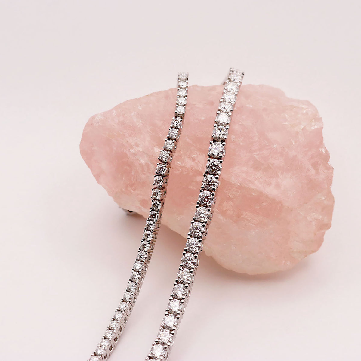 A Moissanite tennis bracelet displayed on a pink crystal stand, showcasing its sparkling diamonds set in a silver band with 18k gold plating.